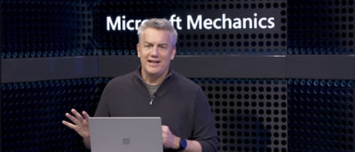 Una persona de pie frente a una pared donde está escrito Microsoft Mechanics 