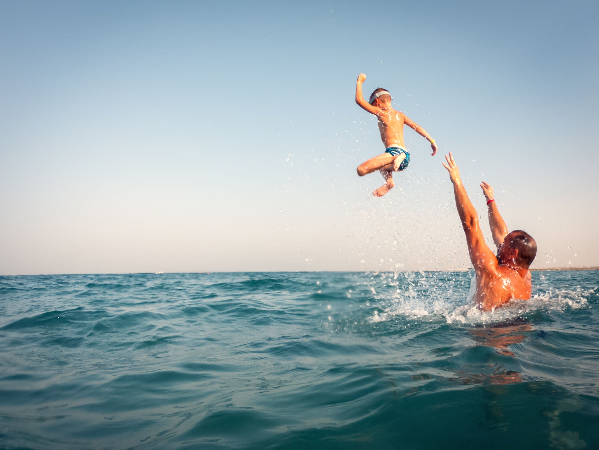 Vater hat Spaß mit seinem Sohn, während er ihn ins Meer wirft