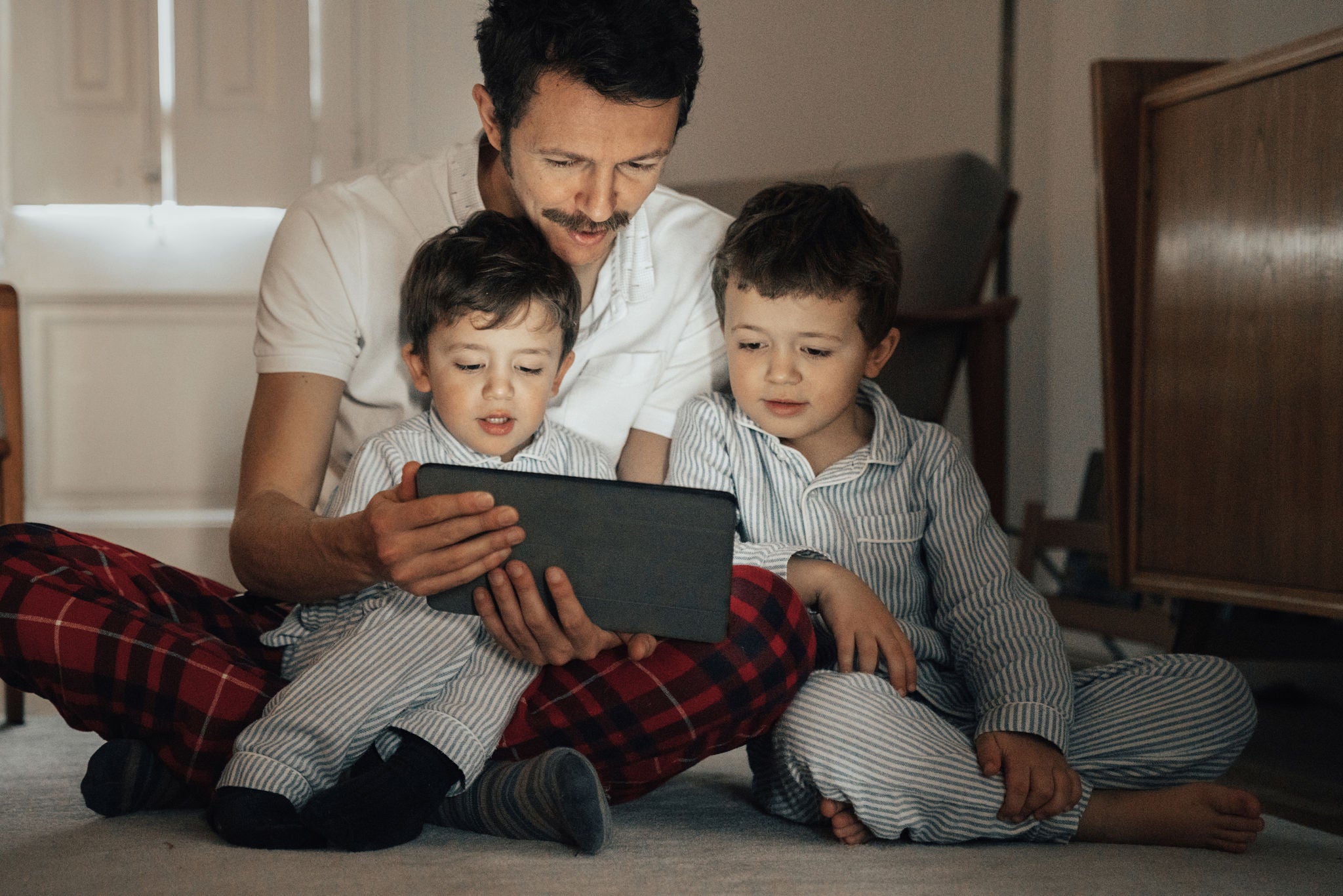 Vater liest seinen zwei kleinen Söhnen Geschichten auf einem Tablet vor