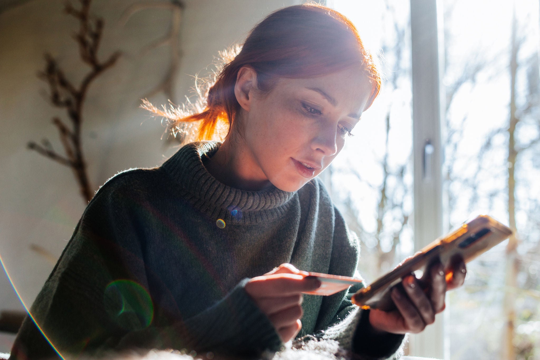 Frau beim Online-Shopping mit Handy und Kreditkarte in der Hand.