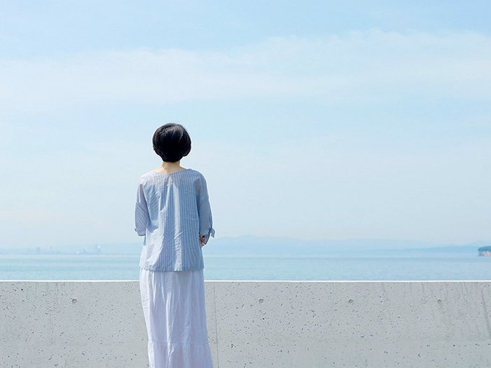 Frau steht an Mauer und blickt auf das Meer und den Horizont